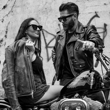 Black-and-white lifestyle photo of a couple wearing BECK® leather jackets, sitting on a Harley motorcycle for vintage rebel aesthetic.