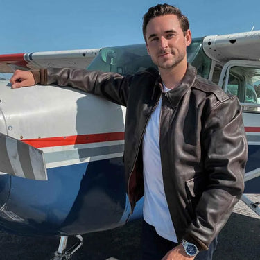 Model wearing Cockpit USA Men's Horsehide A-2 Jacket while standing next to small aircraft