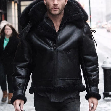 male model wearing the Cockpit USA Black B-3 Hooded Sheepskin Bomber Jacket walking on a snowy city street.