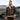 Male model wearing the Cockpit USA Men's Champ Sheepskin Bomber Jacket outdoors near aircraft