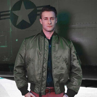 Model wearing Cockpit USA Men's MA-1 Nylon Flight Jacket in olive green in front of military aircraft