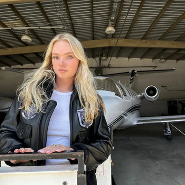 Model wearing the Stealth Top Gun Jacket while standing in front of a private jet in a hangar.