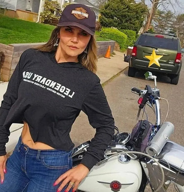 Woman wearing Legendary USA Booty Call cropped hoodie, front view with logo text, standing beside classic motorcycle