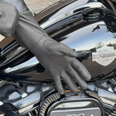 Rider wearing black deerskin gauntlet gloves while resting hand on black Harley-Davidson motorcycle tank
