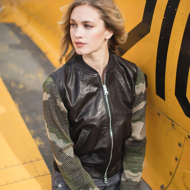 Female model wearing the Hot Stuff bomber jacket beside a vintage yellow aircraft