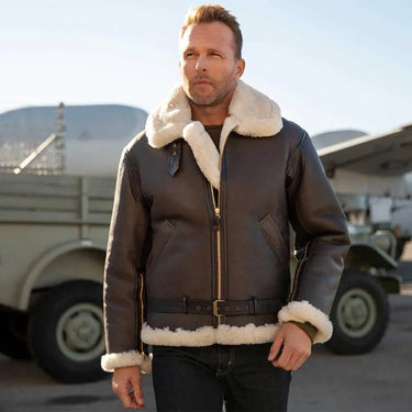 Male model wearing the Cockpit USA Men's Champ Sheepskin Bomber Jacket outdoors near aircraft