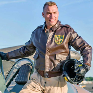 Model wearing Cockpit USA Men's Flying Tigers A-2 Flight Jacket while posing beside a WWII aircraft