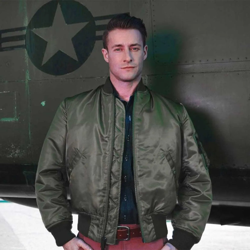 Model wearing Cockpit USA Men's MA-1 Nylon Flight Jacket in olive green in front of military aircraft