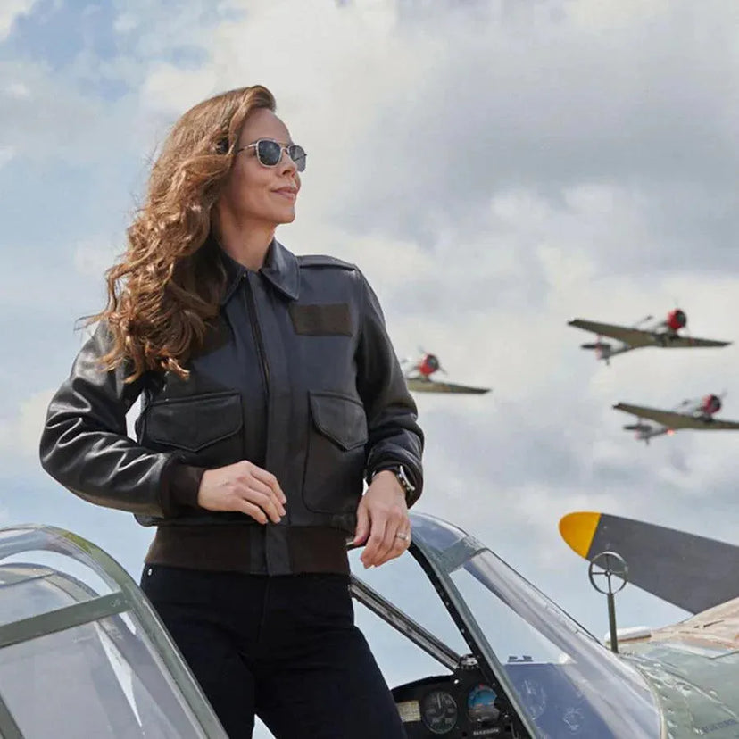 Female model wearing the A-2 Jacket next to a vintage aircraft with planes flying overhead.