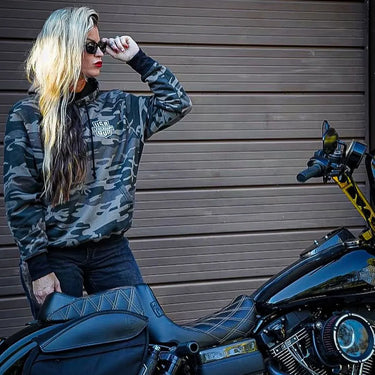 Female rider wearing Legendary Sniper camo motorcycle hoodie while sitting on black motorcycle, lifestyle photo